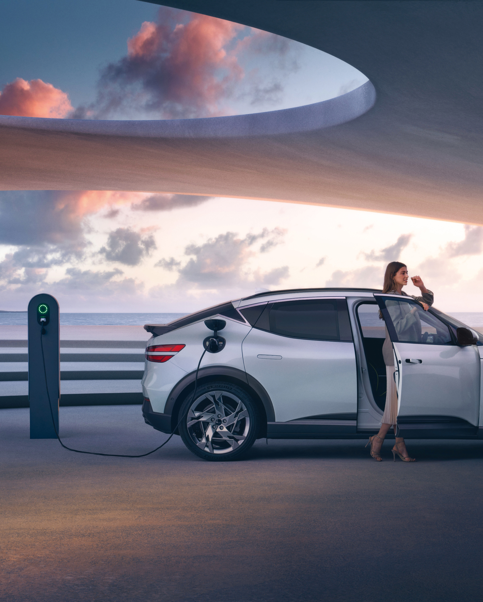 Vue latérale d'un GV60 Blanc Uyuni GV60 en train de charger avec une femme devant la porte du passager. 