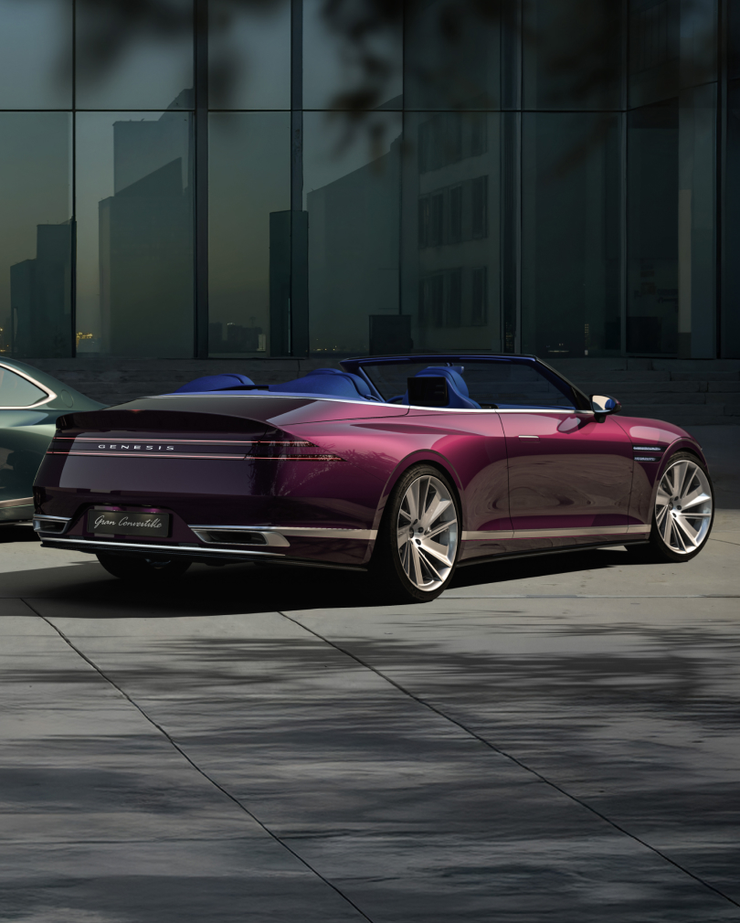 A Genesis X Gran Convertible is parked with the rear facing forward, with a modern city in the background.