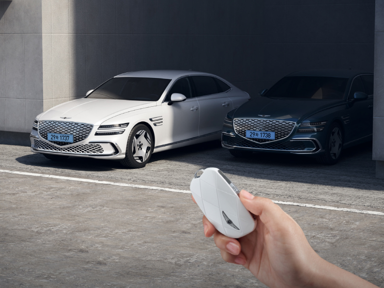 전진 출차하며 그늘진 주차 공간에서 벗어나고 있는 Electrified G80가 보입니다. 그 앞으로는 자동차 키를 쥔 손이 보입니다.