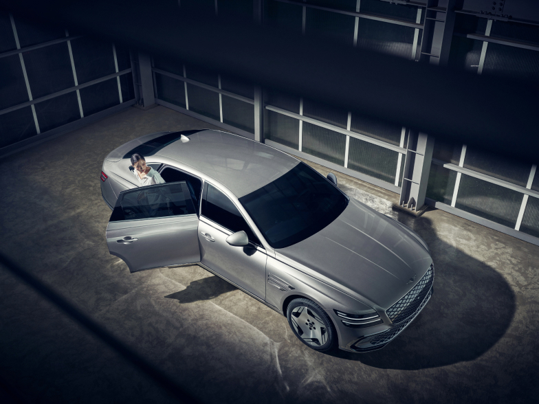 실내 공간에 정차된 Electrified G80의 뒷좌석에서 한 여성이 내리고 있습니다.