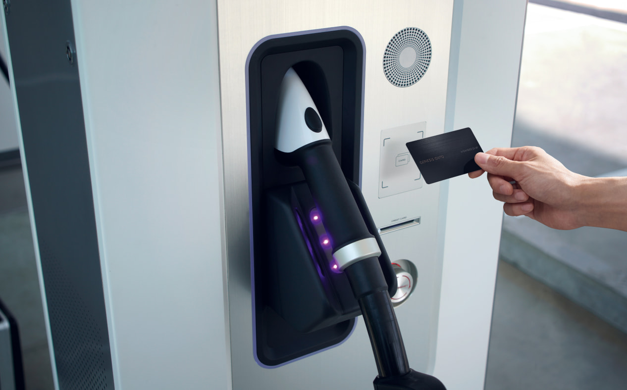 Close-up of a person's hand paying for a recharge by holding a card to the payment terminal at a public charging station.