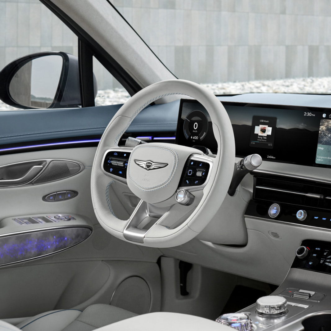 The driver’s seat of the Electrified GV70 is decorated in Icy Blue/Glacier White two-tone interior color, with a white-toned steering wheel in the center of the image.