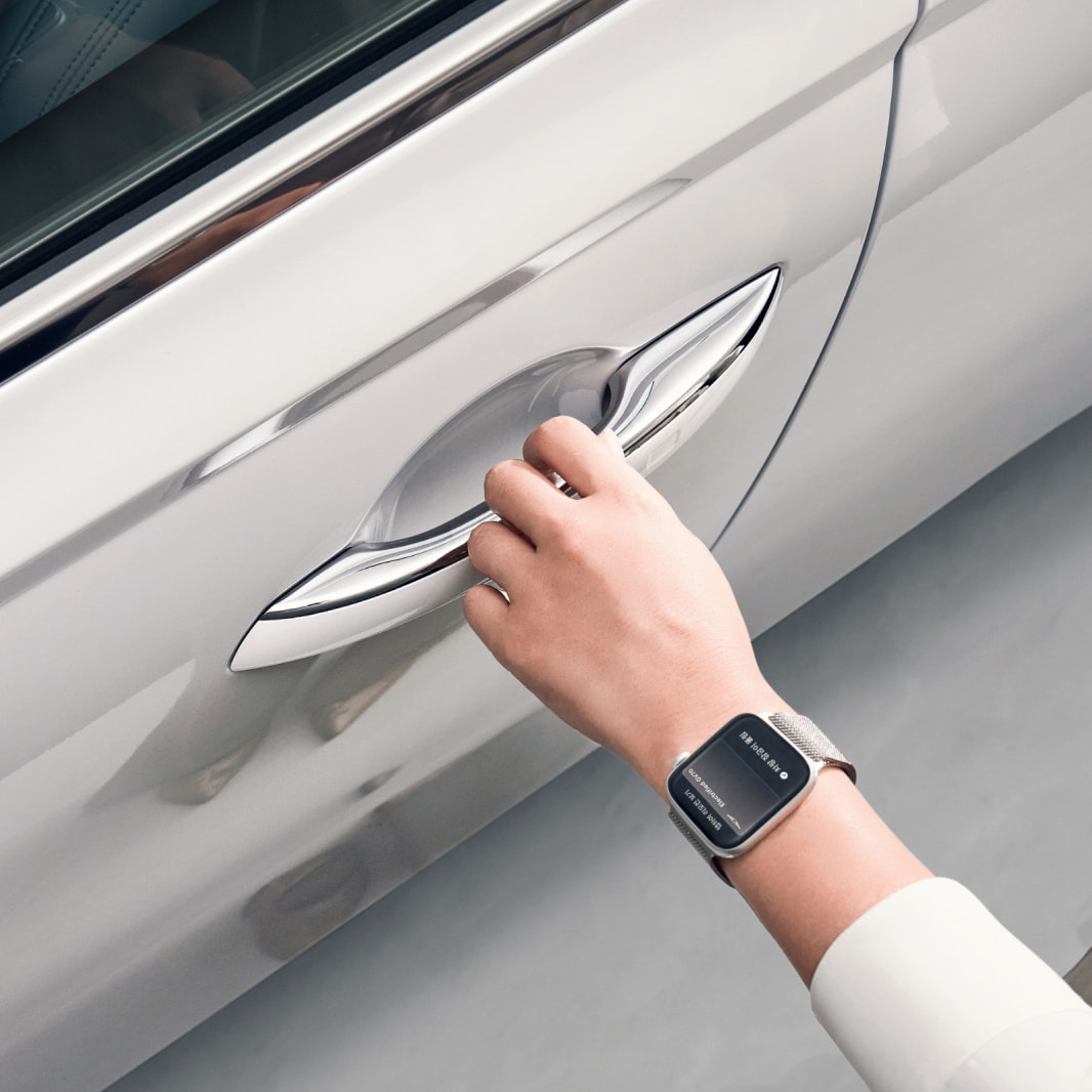 The hand of a person wearing a smartwatch reaches for the door handle.