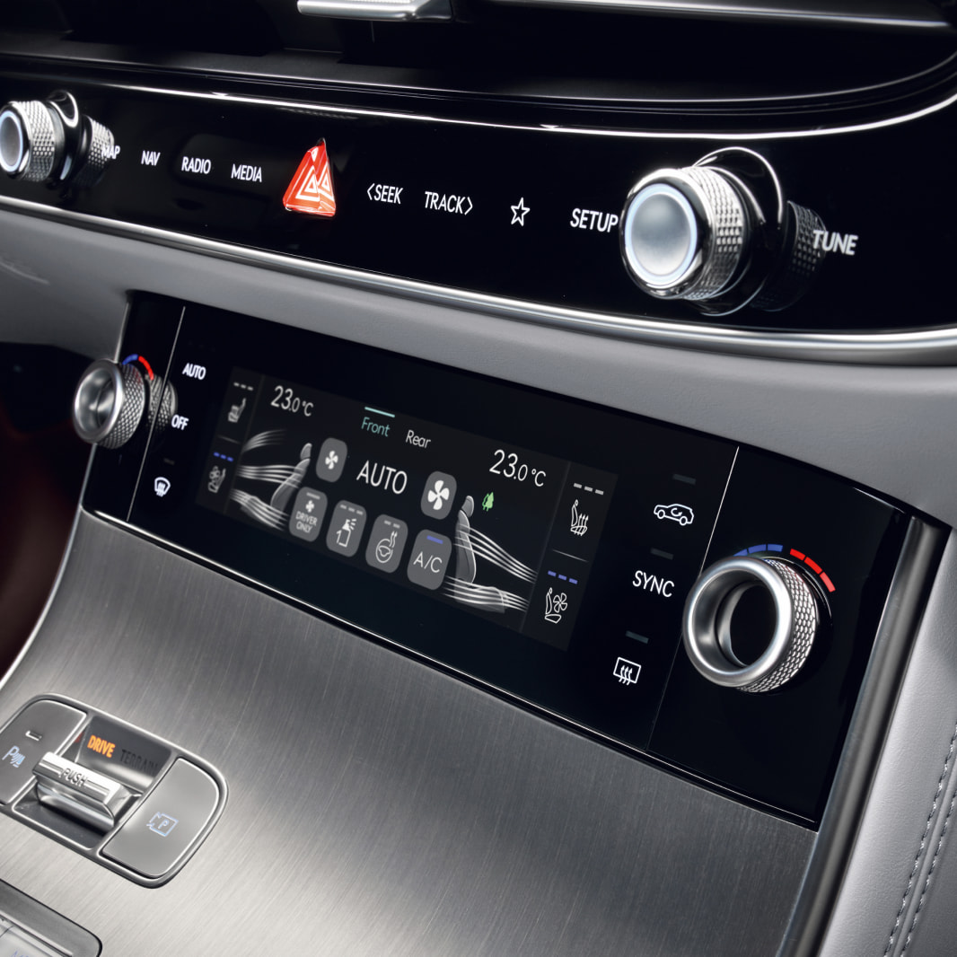 A view of the control panel in the front of the vehicle, featuring touch screens and dials that control ventilation and temperature.