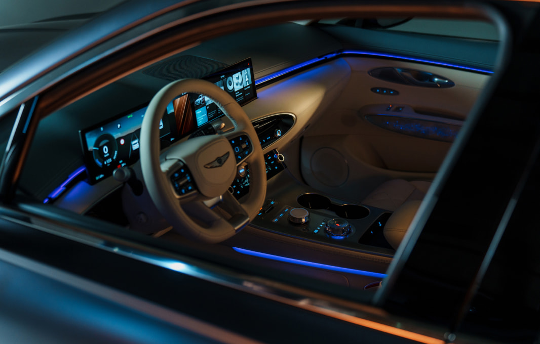 A view of the driver's seat of the Electrified GV70. A wide display in front of the driver's seat is on.