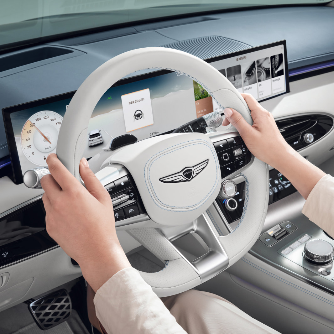 As a driver grips the steering wheel, a warning message appears on the display screen reminding the driver not to let go of the wheel while driving.