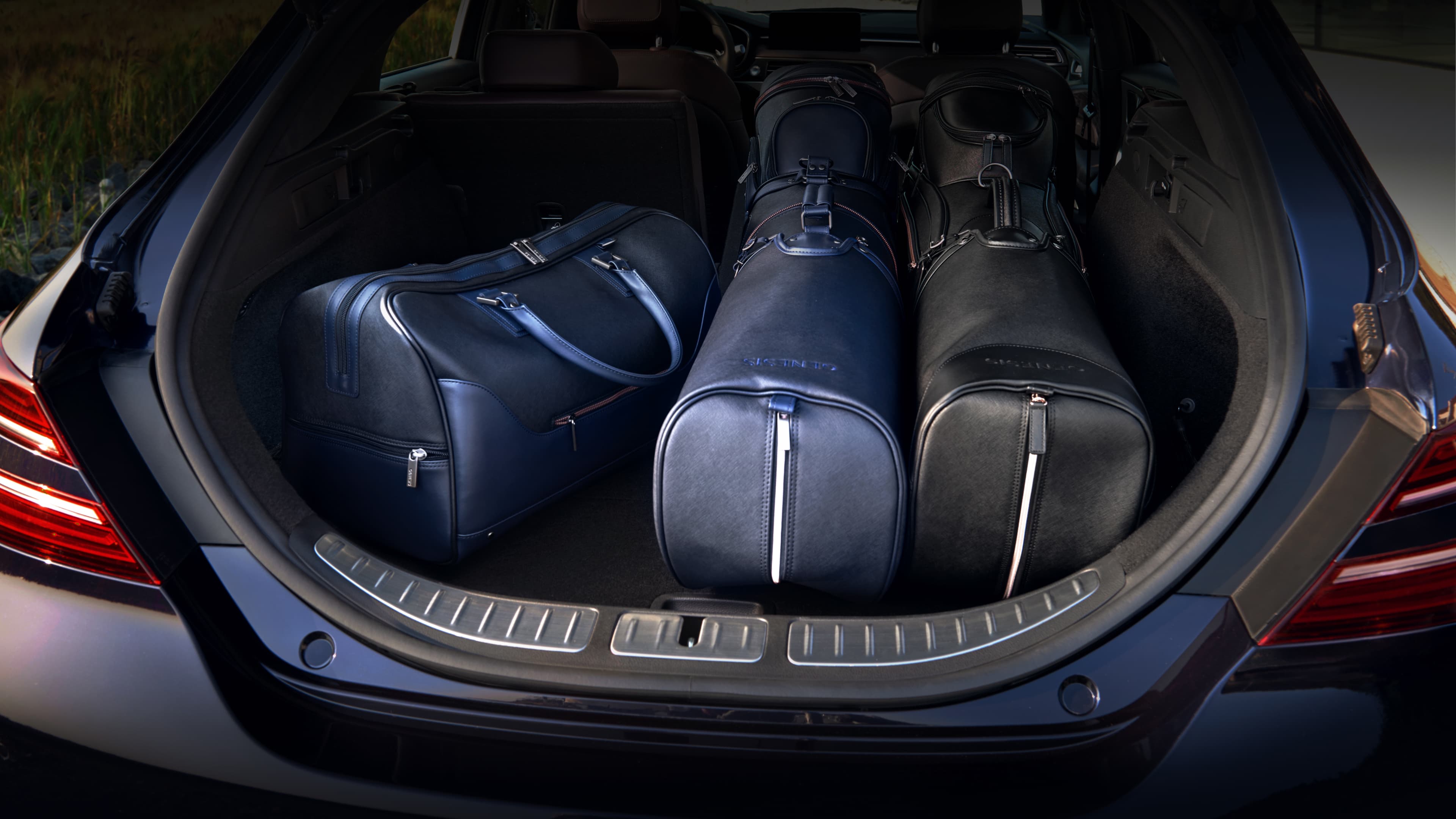 The car's trunk is open and two golf bags and a Boston bag are loaded inside.