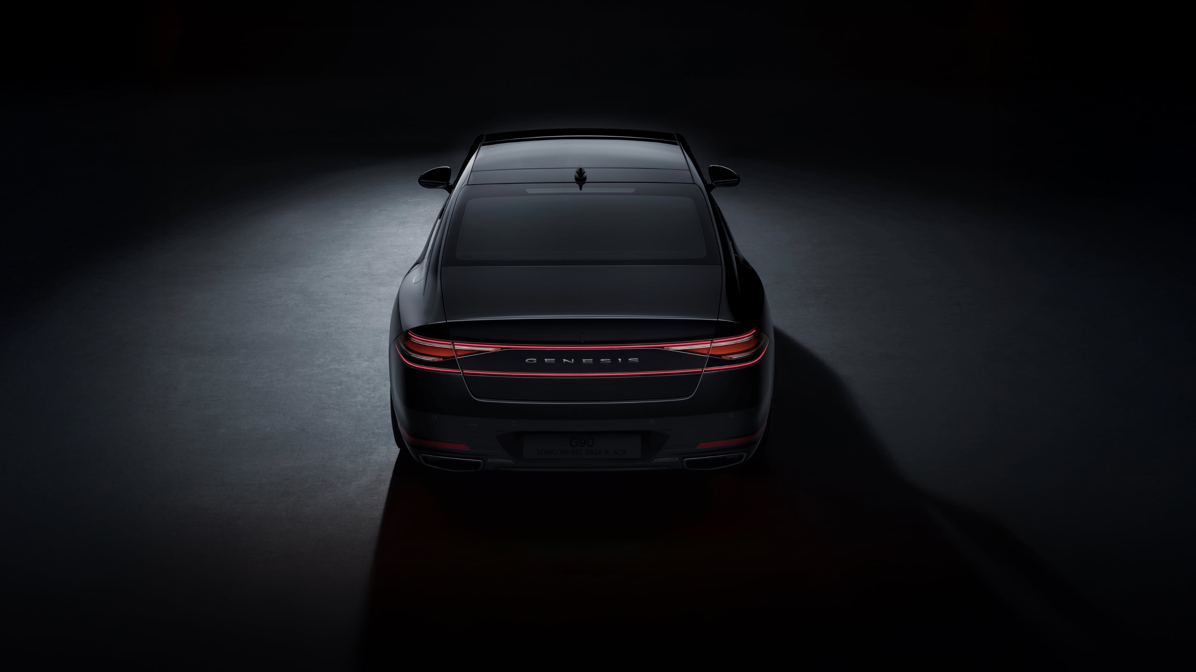 A rear view of the G90 Long Wheel Base Black, parked on illuminated ground in a dark space.