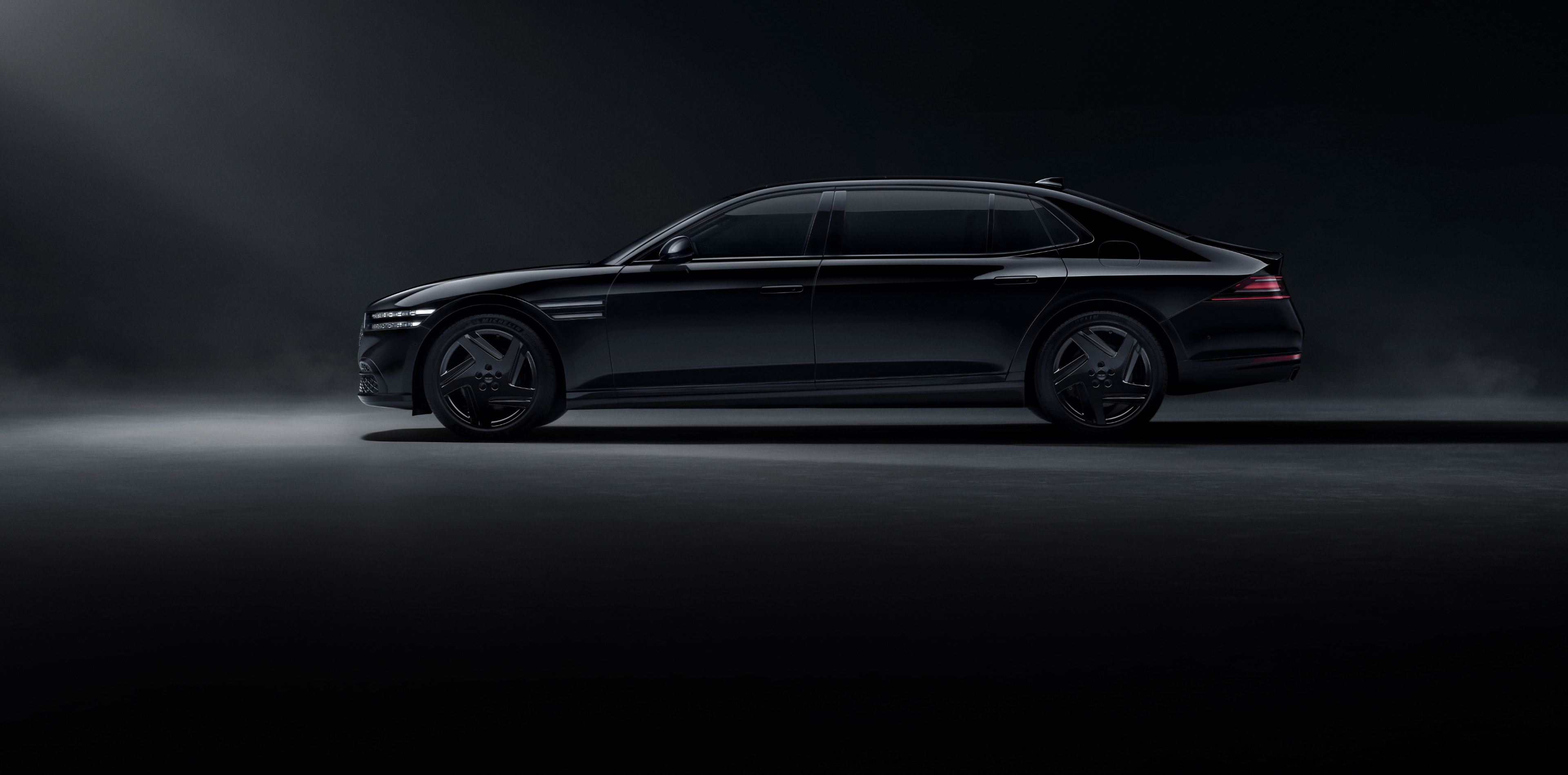 A side view of the G90 Long Wheel Base Black, parked under a spotlight in a dark space.