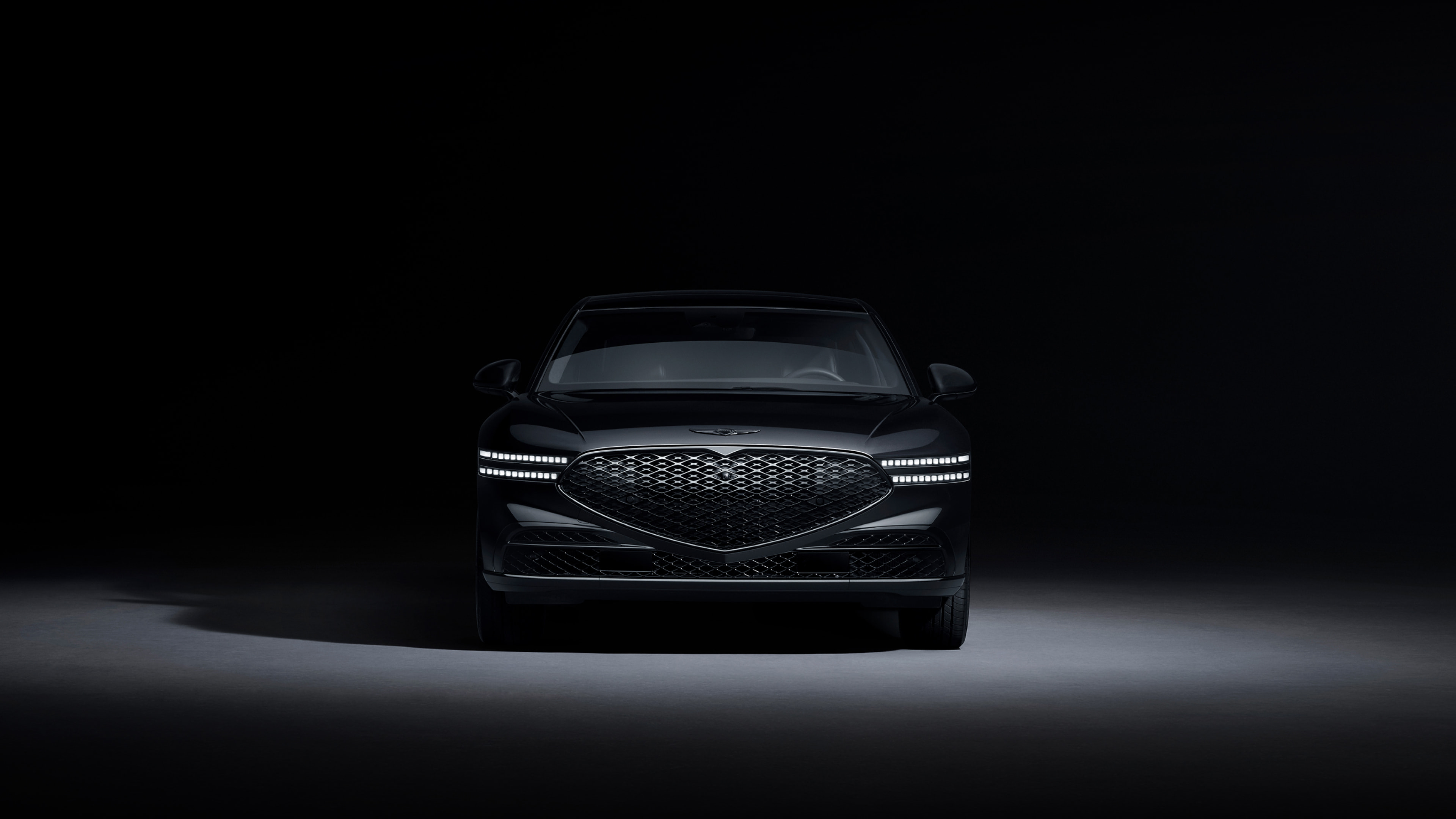 A front view of the G90 Long Wheel Base Black, parked on illuminated ground in a dark space.