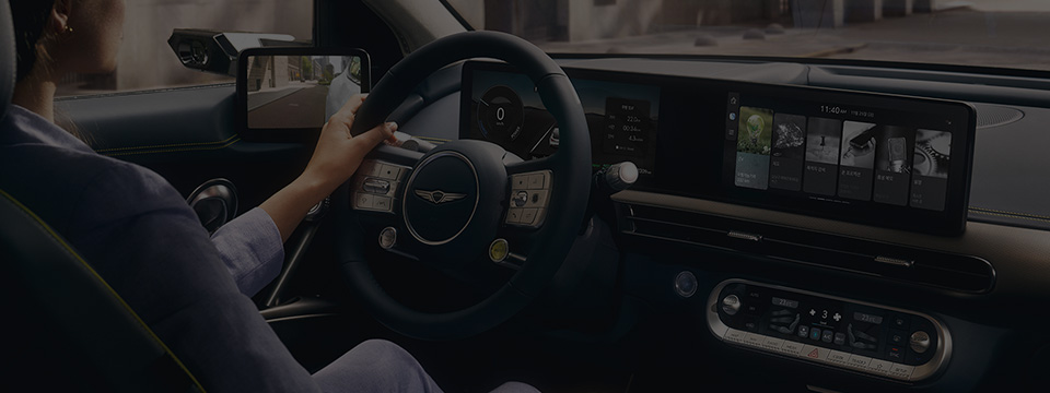 A woman sits in the driver's seat of the Genesis GV60, holds the steering wheel, and sees the spacious interior embodying Genesis' design philosophy.