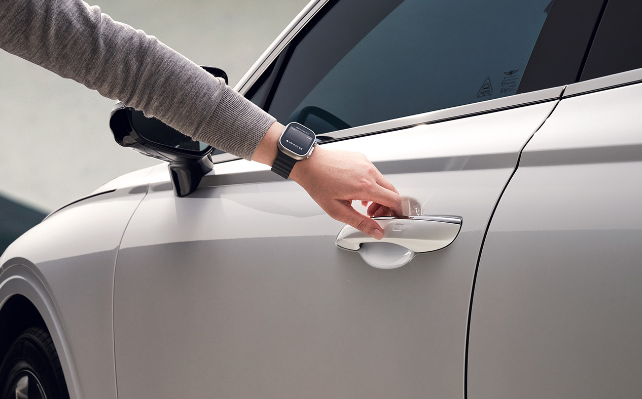 The driver is wearing a smartwatch running the MY GENESIS app and opening the door. 