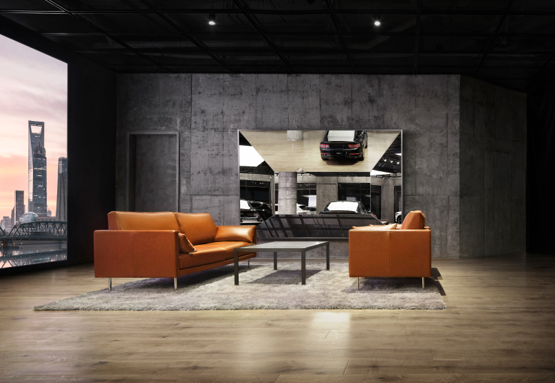 Two brown sofas and a glass table are in front of a dark staircase.