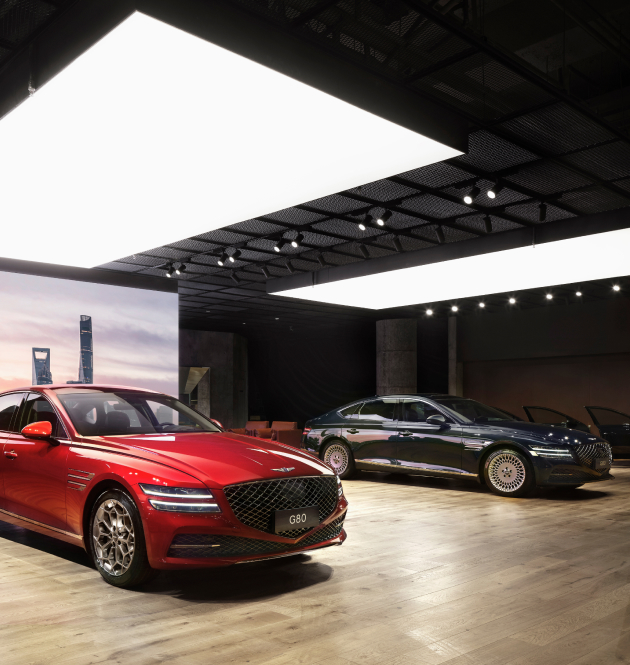 Two Genesis vehicles are on display under wide ceiling lighting.