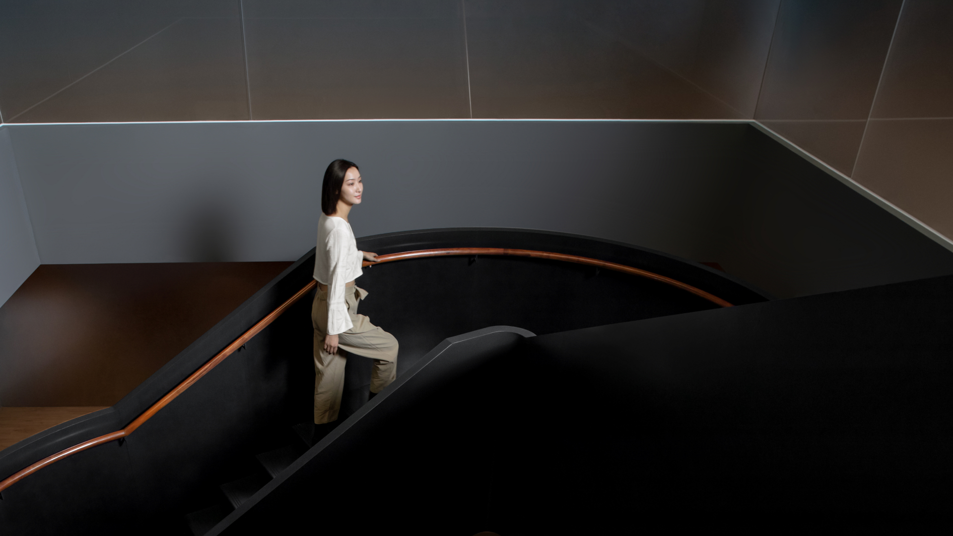 A woman holds a wooden handrail as she goes up the dark staircase.