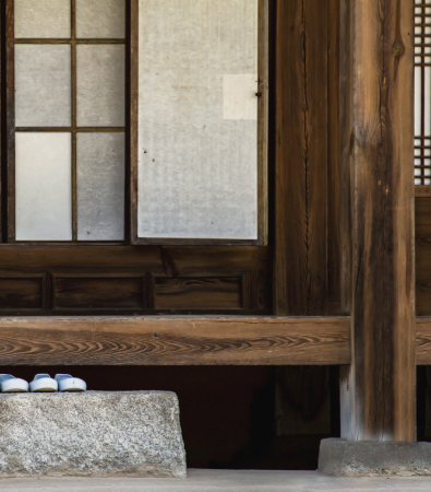 A close-up view of a hanok's veranda and stepping stone in front of sliding wooden doors.