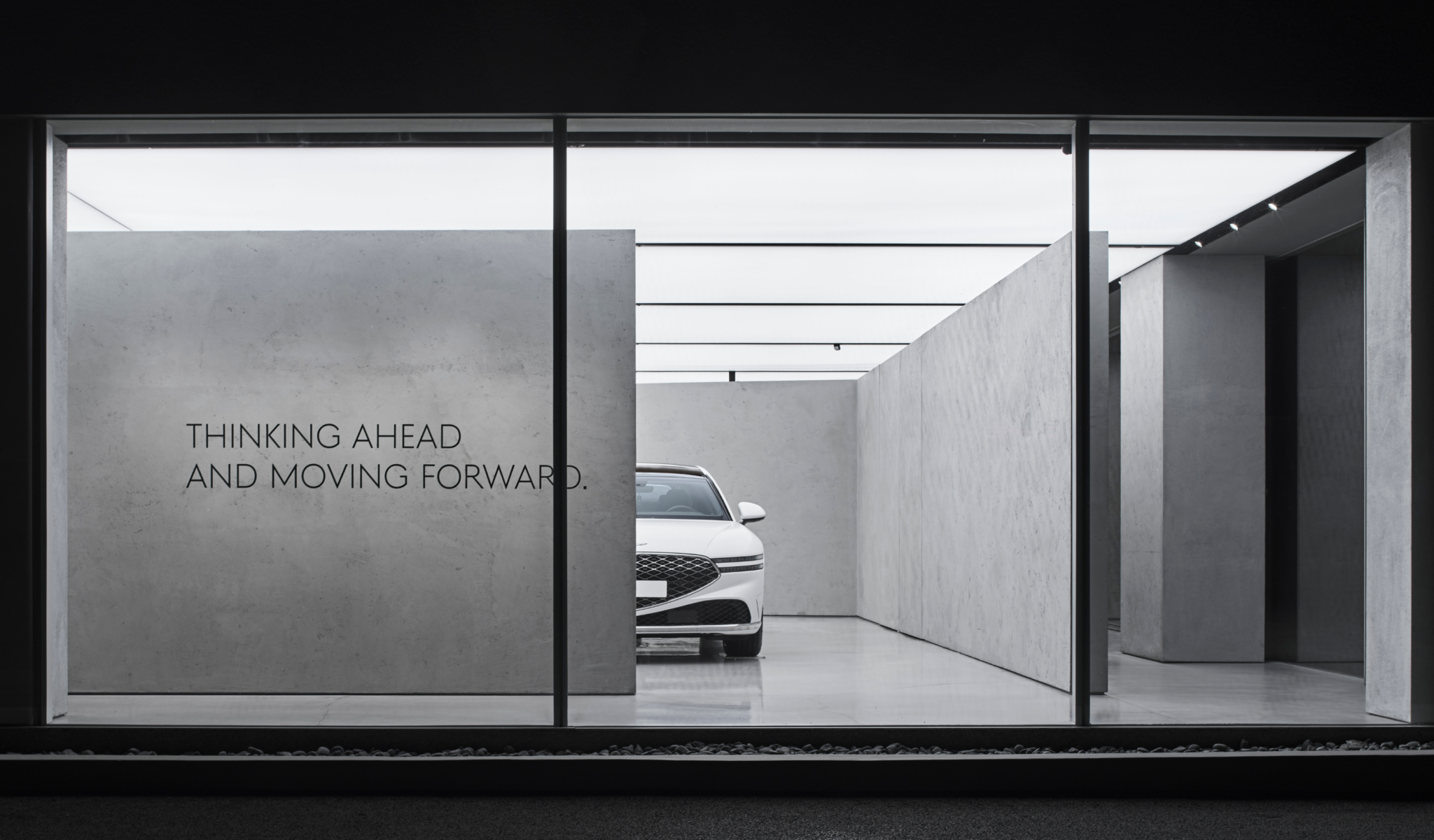 The back half of a black Genesis vehicle sits next to a concrete wall.