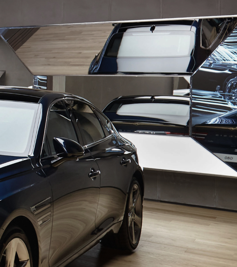 A Genesis vehicle sits in front of a polyhedral mirror. The mirror reflects multiple angles of the vehicle's rear.